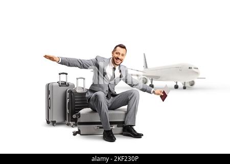 Bussinessman seduto su una valigia di fronte a un aereo e stendendo le braccia isolate su sfondo bianco Foto Stock