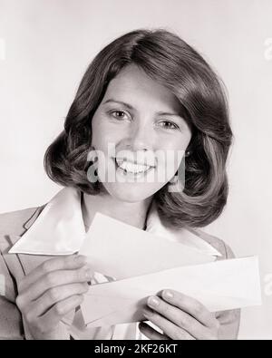 1970S RITRATTO DONNA SORRIDENTE TENENDO APERTA BUSTA RIMUOVERE CONTROLLO SORRIDENTE GUARDANDO LA MACCHINA FOTOGRAFICA - G8579 HAR001 HARS OCCHIO CONTATTO BRUNETTE FELICITÀ ALLEGRA SCOPERTA RIMUOVERE ECCITAZIONE HAIRSTYLE VRIDE PAGAMENTO SORRISI GIOIOSO ELEGANTE DONNE D'AFFARI BENEFICIO MID-ADULT DONNA MID-ADULT NERO E BIANCO ETNICITÀ CAUCASICA HAR001 VECCHIO STILE PAGINA RAGAZZO Foto Stock