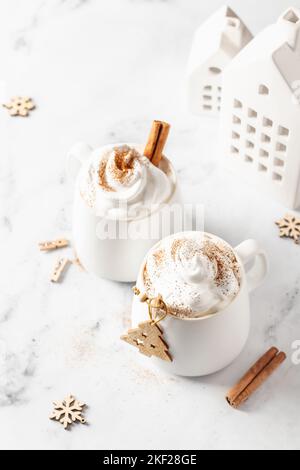 Due tazze di cioccolata calda o cacao con panna montata e cannella su sfondo di marmo bianco da vicino. Xmas mock up, festa card. Cristo tradizionale Foto Stock
