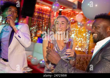 Tre amici maschi e femmine felici e diversi che bevono bicchieri di champagne in una discoteca Foto Stock