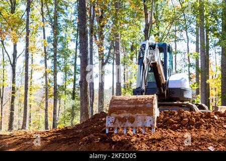 La benna dell'escavatore scava terra sul cantiere edile vicino alla foresta Foto Stock