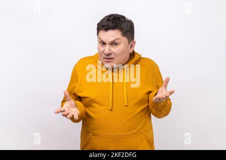 Cosa. Ritratto di uomo di mezza età confuso o scioccato in piedi con le braccia sollevate e guardando la macchina fotografica chiedendo, indossando felpa con cappuccio stile urbano. Studio in interni isolato su sfondo bianco. Foto Stock