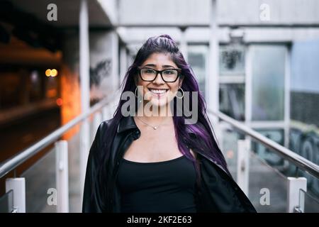 latina ragazza con lunghi occhiali da capelli bruna pelliccia giacca collana sul collo intorno orecchini labbro piercing sorridente a macchina fotografica a piedi sul passaggio urbano Foto Stock