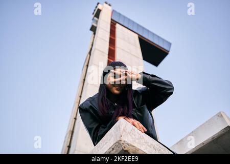 brunette latina ragazza con pelliccia giacca orecchini grandi guardando la fotocamera con la mano sinistra che copre l'occhio sinistro sorridendo alla fotocamera che si trova a terra nel Foto Stock