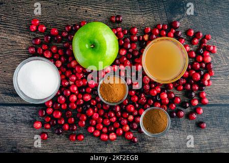 Salsa di mirtilli rossi di mele con sidro e cannella su uno sfondo di legno: Mirtilli rossi freschi, mele e altri ingredienti per salsa di mirtilli rossi Foto Stock