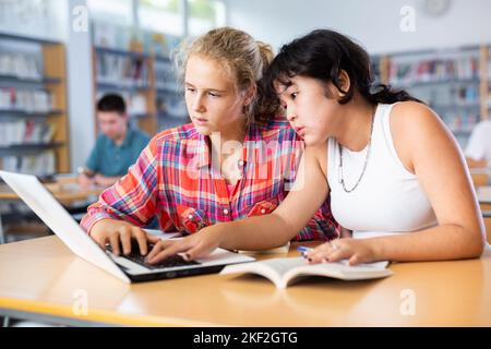 Ritratto di studentessa asiatica con un'amica spagnola che studia in biblioteca utilizzando il computer portatile Foto Stock