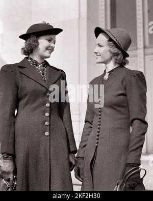 1940S DUE DONNE SORRIDENTI CHE PARLANO SU STREET ALLA MODA VESTITO IN ABITI AUTUNNALI CAPPOTTI LEGGERI E GUANTI - S8531 HAR001 HARS COMUNICAZIONE BIONDA AMICO GIOVANE ADULTO FELICE GIOIA STILE DI VITA DONNE CAPPOTTI COPIA SPAZIO AMICIZIA MEZZA LUNGHEZZA SIGNORE PERSONE FIDUCIA B&W. INCONTRA GLI STILI DI FELICITÀ BRUNETTE E GLI OUTFIT LOW ANGLE DI NETWORKING PER SORRIDE CONNESSIONE DI ALTA CLASSE ALLA MODA AMICHEVOLE GIOIOSO ELEGANTE COOPERAZIONE MODA INSIEME GIOVANE DONNA ADULTA NERA E BIANCA ETNIA CAUCASICA HAR001 VECCHIO STILE Foto Stock