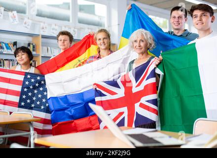 Gruppo di scolaresche con un'insegnante femminile che detiene bandiere nazionali di diversi paesi Foto Stock