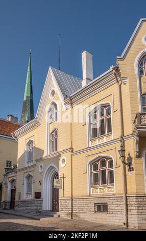 Estonia, Tallinn - 21 luglio 2022: Centro di letteratura per bambini estone facciata anteriore gialla e ingresso principale sotto il cielo blu. Guglia verde di St. OLAF Foto Stock