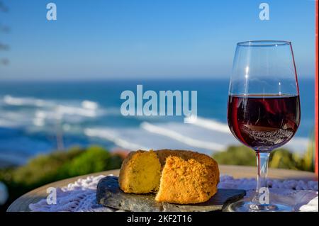 Abbinamento di cibo e bevande portoghesi, bicchiere di vino porto bruno e coccodrillo pastais de bacalhau, servito all'aperto con vista sul blu soleggiato Atla Foto Stock