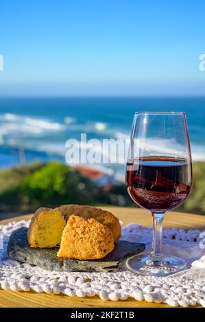 Abbinamento di cibo e bevande portoghesi, bicchiere di vino porto bruno e coccodrillo pastais de bacalhau, servito all'aperto con vista sul blu soleggiato Atla Foto Stock