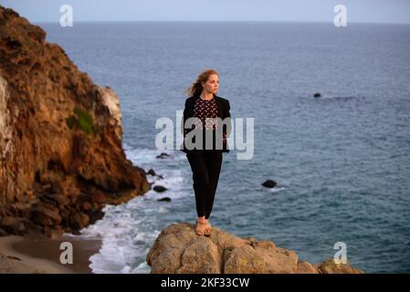 Donna d'affari vincitrice della vita. Leader ragazza a scogliera. Tramonto alba. Femmina di successo. Foto Stock