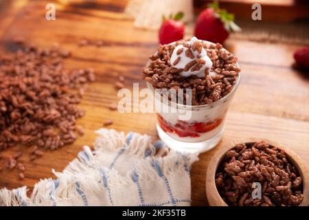 Una sana colazione di yogurt greco con frutta fresca e riso soffiato al cioccolato su un rustico tavolo di legno. Foto Stock