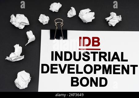 Concetto industriale. Su uno sfondo nero, ci sono pezzi di carta e carta stropicciati con l'iscrizione - Industrial Development Bond Foto Stock