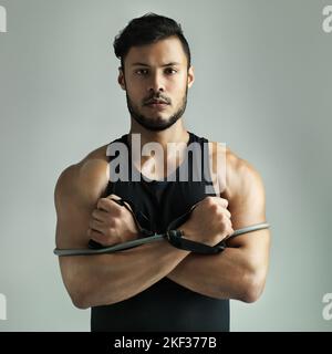 Pronto per un po' di allenamento di resistenza. Studio di un giovane che lavora con una fascia di resistenza su uno sfondo grigio. Foto Stock