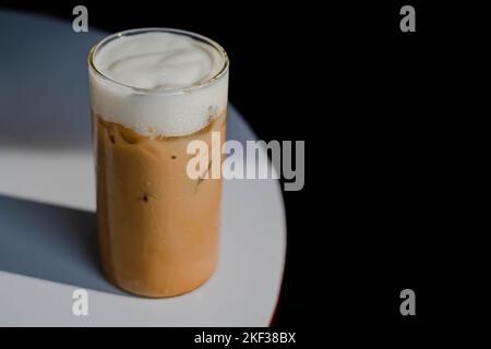 Latte di caffè o cappuccino servito in un bicchiere su un tavolo bianco con sfondo scuro Foto Stock