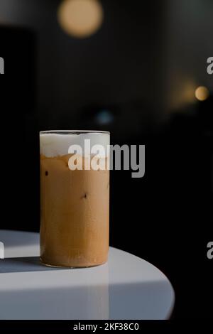 Latte di caffè o cappuccino servito in un bicchiere su un tavolo bianco con sfondo scuro Foto Stock