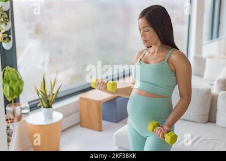 Gravidanza fitness. Donna incinta esercizio di allenamento domestico esercizio di forza fitness con pesi a manubri. Il braccio per l'allenamento del corpo si arriccia mostrando la pancia e un Foto Stock