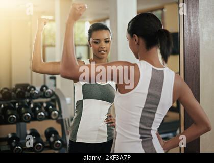 Mantenere la forma della punta. Una giovane donna che flette i muscoli davanti allo specchio in palestra. Foto Stock