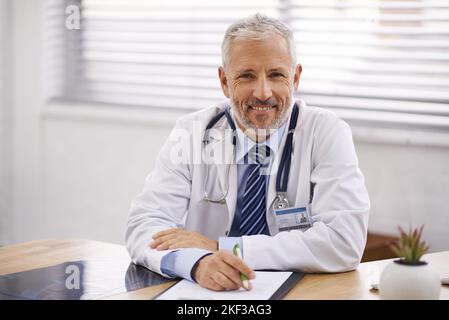 Il medico la vedrà ora. Ritratto di un medico maschio maturo seduto alla sua scrivania. Foto Stock