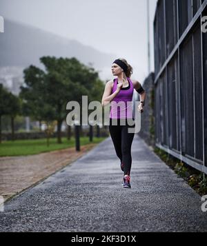 Shes determinato a raggiungere i suoi obiettivi di fitness. Una giovane donna che corre lungo un percorso. Foto Stock