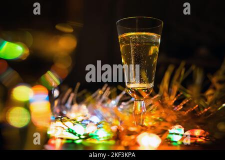 Un bicchiere di champagne sul tavolo sulle decorazioni natalizie. La celebrazione del Natale. Luci di colore elettriche riflesse in un bicchiere di vino Foto Stock