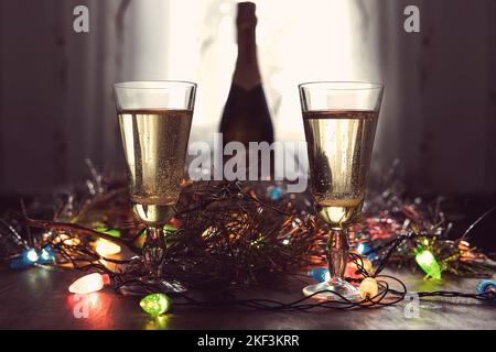Due bicchieri di champagne e bottiglia su un tavolo in legno decorata con accessori di Natale per festeggiare il nuovo anno e di Natale. Serata romantica Foto Stock