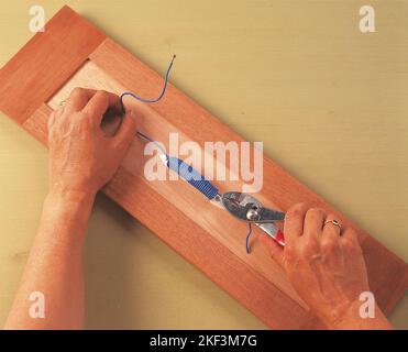 Tirare la coda del filo con un paio di pinze Foto Stock