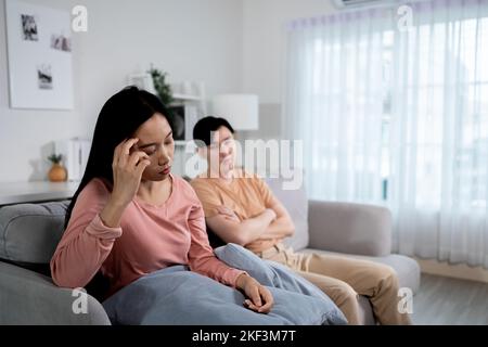 Rovesciato ragazzo asiatico e ragazza seduta insieme sul divano a casa dopo aver litigato e combattere a casa. Offeso coppia sposata in silenzio dopo problema di relazione Foto Stock