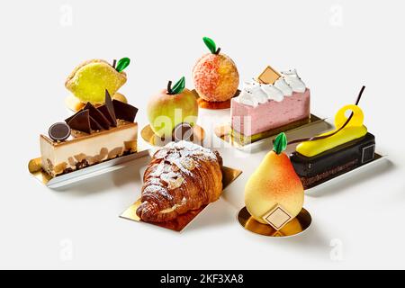 Dolci a forma di frutta al forno, mousse e fette di torta al cioccolato, croissant al soffio su sfondo bianco Foto Stock