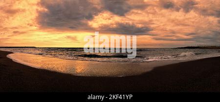 Tramonto panoramico color arancio pastello sulla spiaggia con cielo stellato con nuvole di cumuli e onde di mare ruvide che si infrangono sulla riva con una rilassante risata Foto Stock
