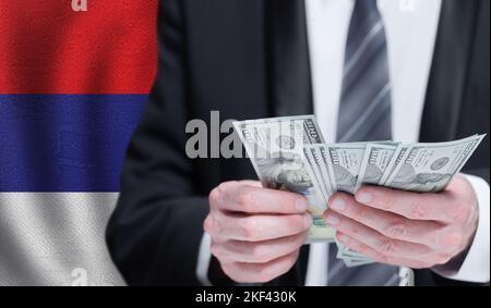 Mani che detengono denaro in dollari sulla bandiera della Serbia Foto Stock
