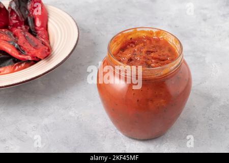 Vasetto di vetro di deliziosa Ljutenica fatto di peperoni arrostiti su fondo grigio neutro. Cibo balcanico Foto Stock