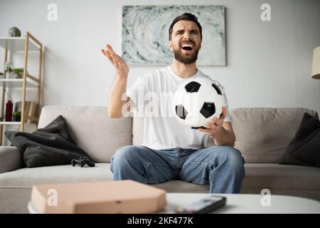 KIEV, UCRAINA - 21 OTTOBRE 2022: Dispiaciuto uomo che tiene il calcio e guarda il campionato a casa, immagine di borsa Foto Stock