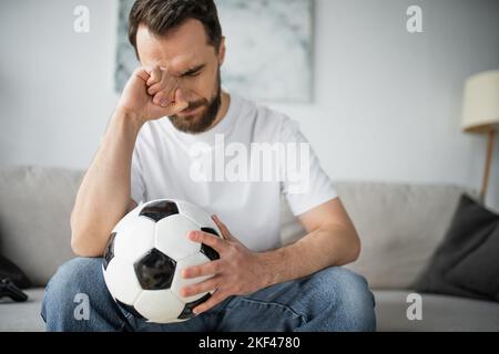 KIEV, UCRAINA - 21 OTTOBRE 2022: Uomo sconvolto che tiene il calcio dopo aver guardato il campionato a casa, immagine di borsa Foto Stock