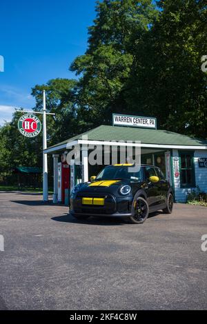 Warren Center, PA, USA - 24 settembre 2022: Un mini Cooper se 2023 nero e giallo, un veicolo elettrico, è fotografato vicino ad una stazione di benzina vintage locate Foto Stock