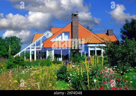 Modernes Einfimilienhaus mit Wintergarten, Grüner Garten mit Blumen im Vordergrund, Foto Stock