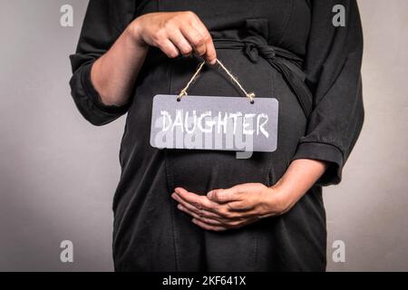 Figlia. Donna incinta tiene una scheda in miniatura con un testo. Foto Stock