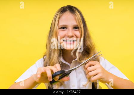 Ragazza scolastica adolescente con forbici, isolata su sfondo giallo. Creatività dei bambini, arti e mestieri. Foto Stock