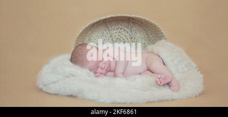 Ripresa del neonato in studio estetico - carino il bambino che dorme pacefoly in una pelliccia fuori del cestino in uno sfondo beige Foto Stock