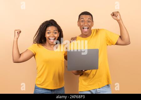 Concetto di grande vittoria. Una coppia nera con un laptop che si è gioita, festeggia la vittoria e scoppia pugni arroccati Foto Stock