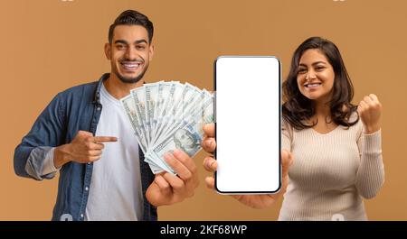 Uomo e donna arabi con grande gioia che celebrano la vittoria, mostrando smartphone, denaro contante Foto Stock