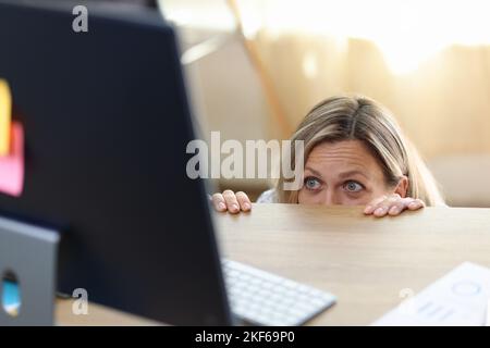 Donna spaventata e scioccata nel panico dietro la scrivania guardando lo schermo del computer. Foto Stock