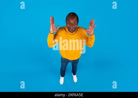 Vista ad angolo alto dell'emotivo uomo nero che alza le mani Foto Stock