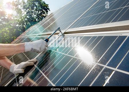 La mano di un lavoratore si avvita pannelli solari con bellissimi riflessi solari e lenti svasate su un tetto con Foto Stock