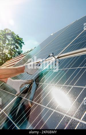 La mano di un lavoratore si avvita pannelli solari con bellissimi riflessi solari e lenti svasate su un tetto con Foto Stock
