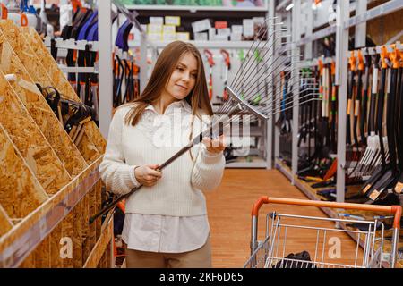 Giovane donna sceglie un rastrello in un reparto di giardinaggio di deposito di ferramenta Foto Stock
