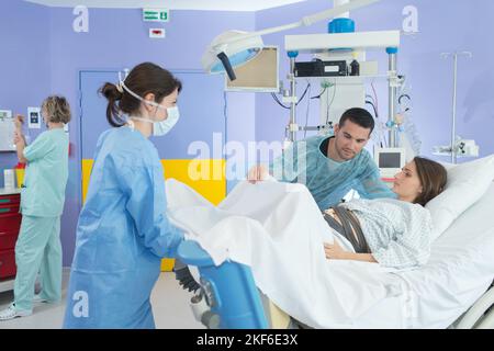 il marito del team medico che guarda la donna durante la consegna in sala operatoria Foto Stock