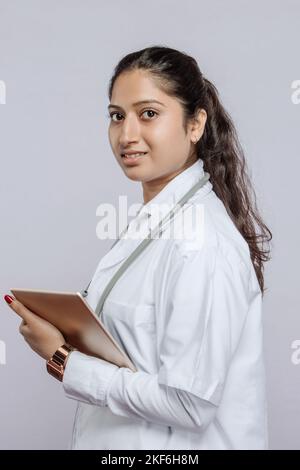 Un ritratto di una dottoressa sudasiatica che tiene una tavoletta su sfondo grigio Foto Stock