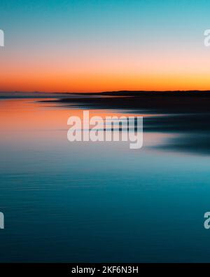 Uno scatto verticale di un cielo sfumato durante il tramonto che si riflette perfettamente sull'acqua con silhouette di terra - ottimo per poster, frasi, citazioni sfondo Foto Stock